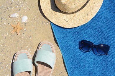 Photo of Stylish slippers, straw hat, sunglasses and blue towel on sand, flat lay. Beach accessories