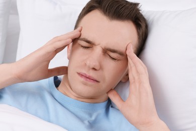 Photo of Sad man suffering from headache in bed indoors