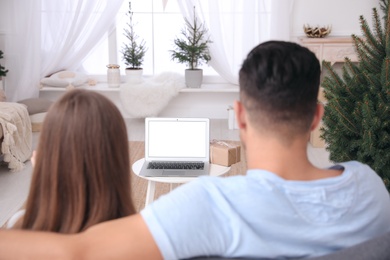 Photo of Couple using video chat on laptop in room decorated for Christmas