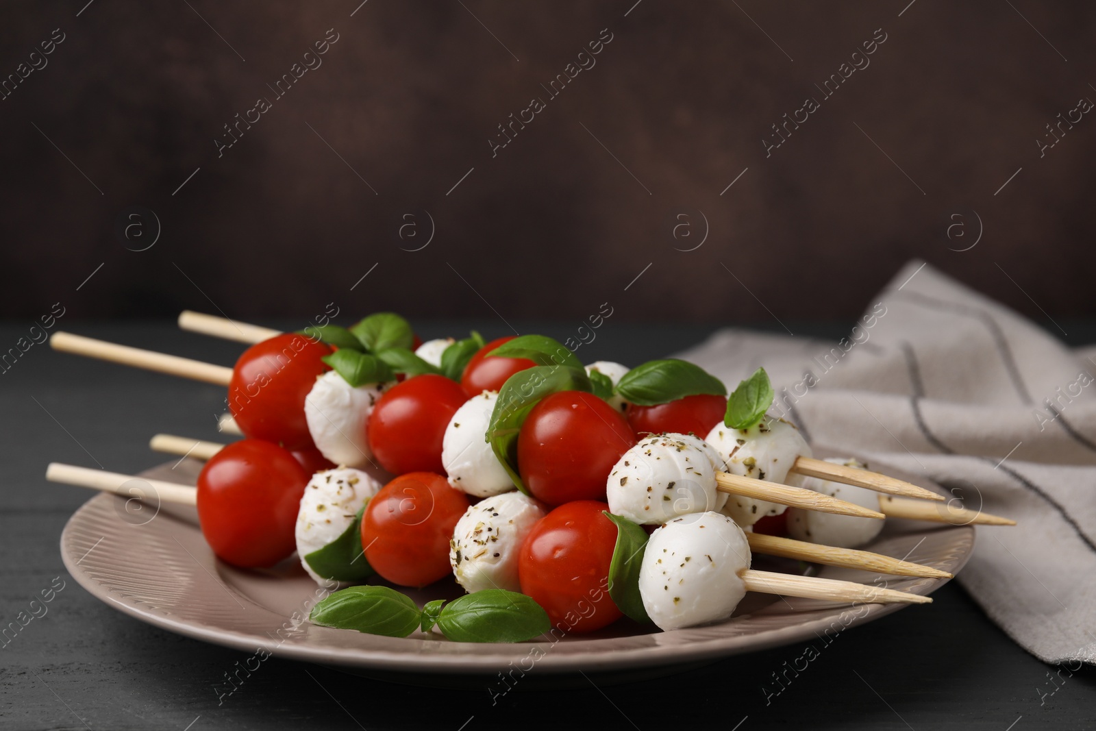Photo of Caprese skewers with tomatoes, mozzarella balls, basil and spices on grey wooden table, closeup