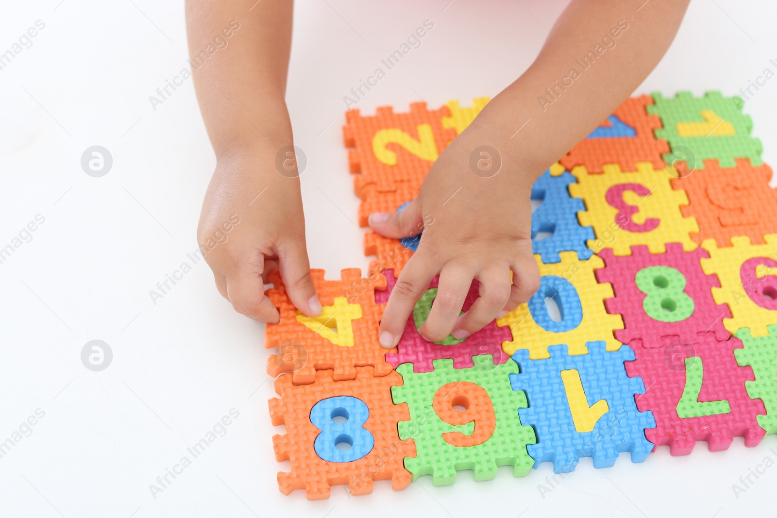 Photo of Little girl playing with colorful puzzles at white table, closeup. Educational toy