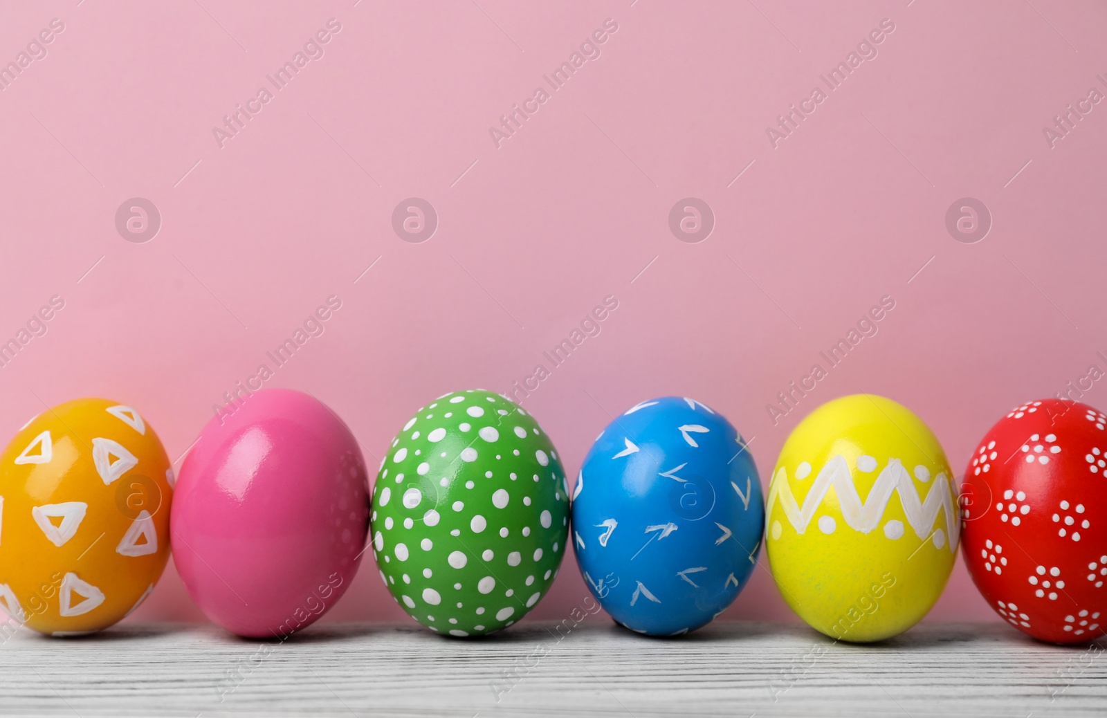 Photo of Decorated Easter eggs on table near color wall. Space for text