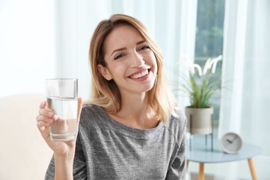 Photo of Young woman holding glass with clean water at home