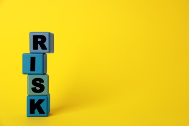 Photo of Word Risk made of colorful cubes on yellow background, space for text