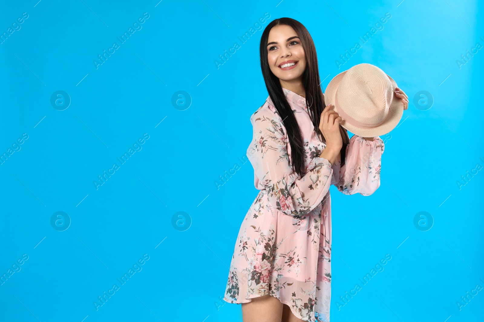 Photo of Young woman wearing floral print dress with straw hat on light blue background. Space for text