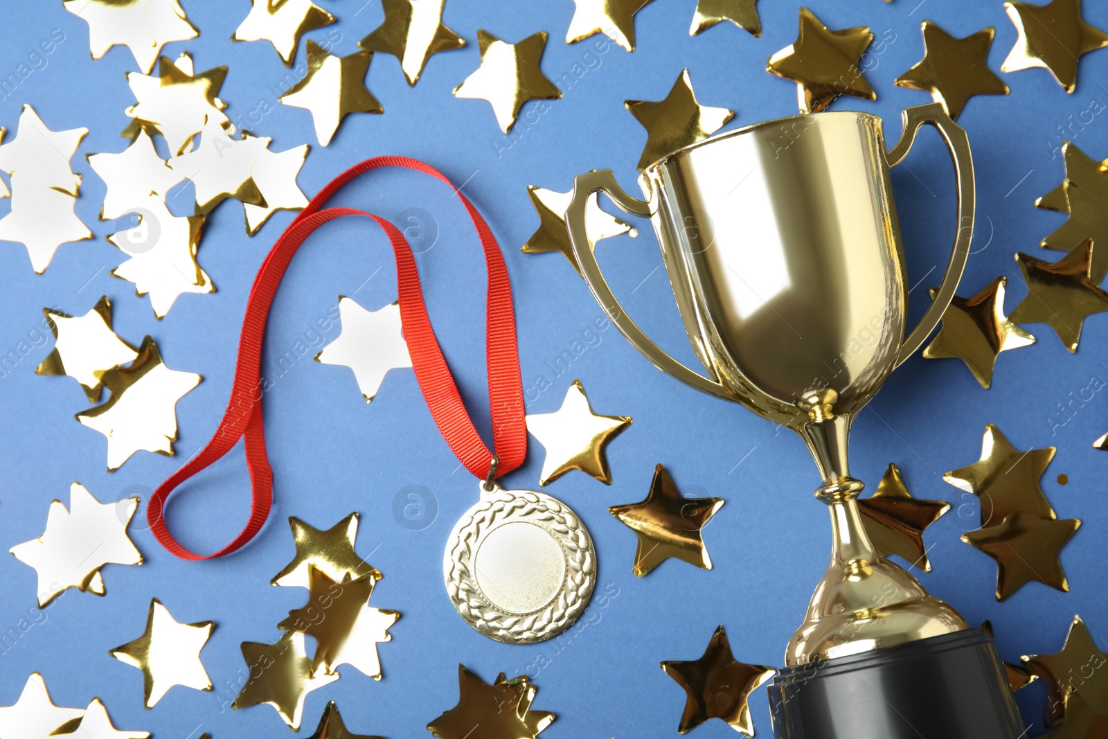 Photo of Gold trophy cup, medal and confetti on blue background, flat lay