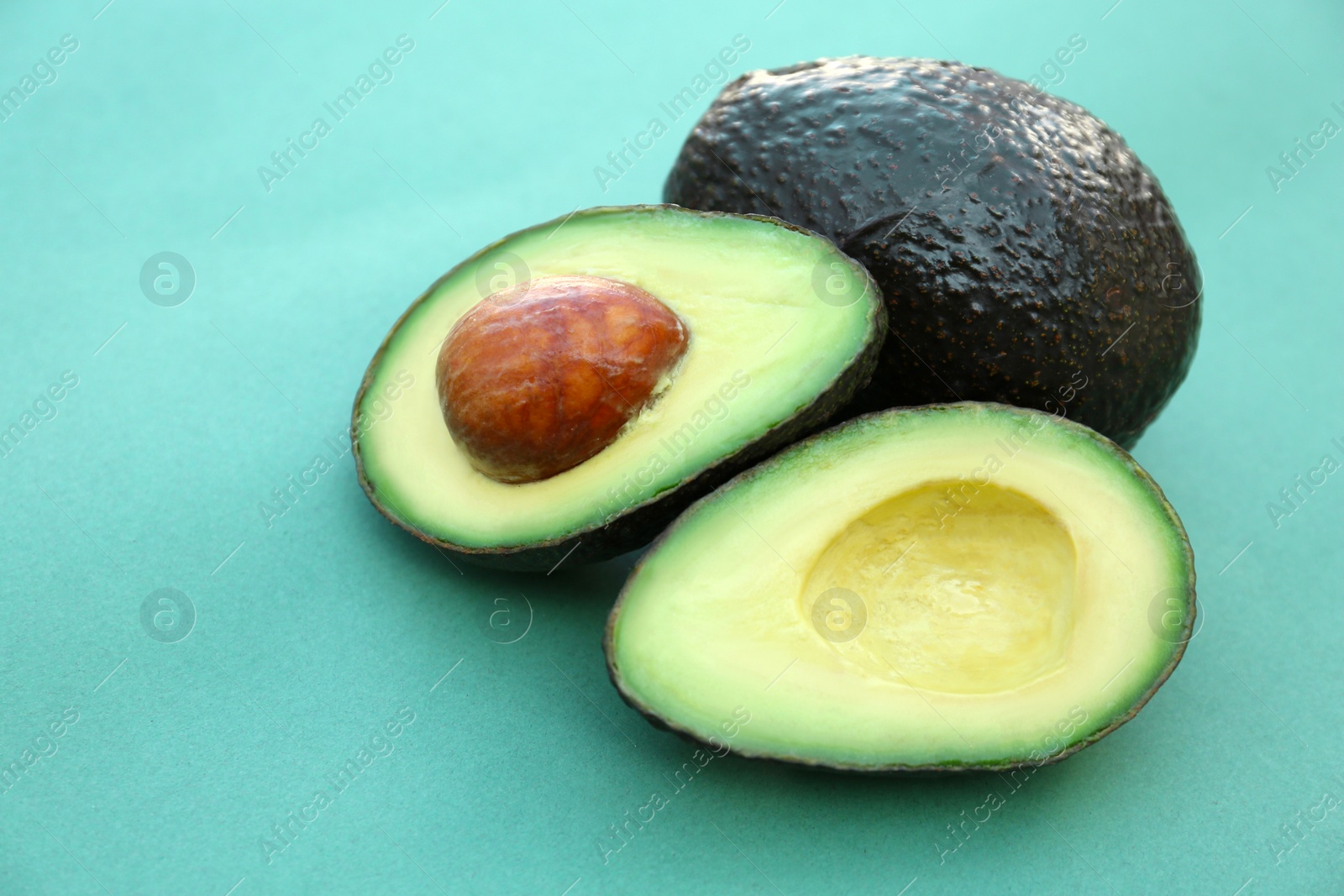 Photo of Tasty whole and cut avocados on turquoise background