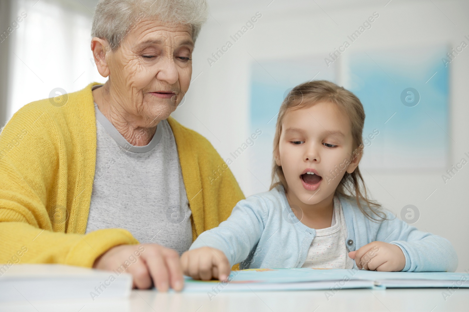 Photo of Cute girl and her grandmother reading book at home