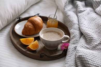 Wooden tray with delicious breakfast and beautiful flower on bed indoors