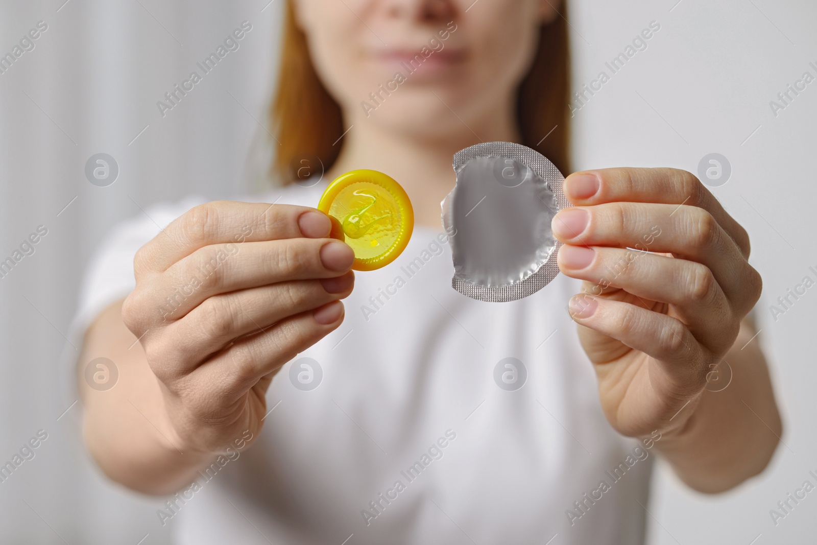 Photo of Woman holding unwrapped condom indoors, closeup. Safe sex