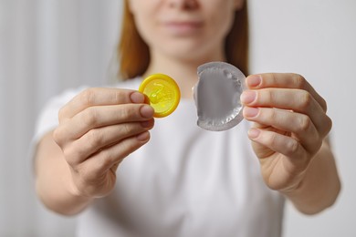 Woman holding unwrapped condom indoors, closeup. Safe sex