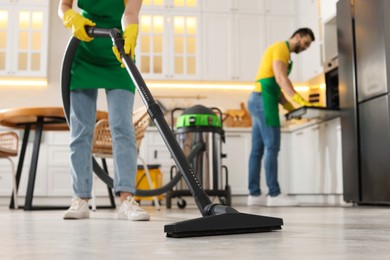 Photo of Professional janitor vacuuming floor in kitchen, closeup