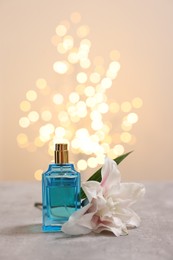 Photo of Bottle of perfume and beautiful lily flower on table against beige background with blurred lights, space for text