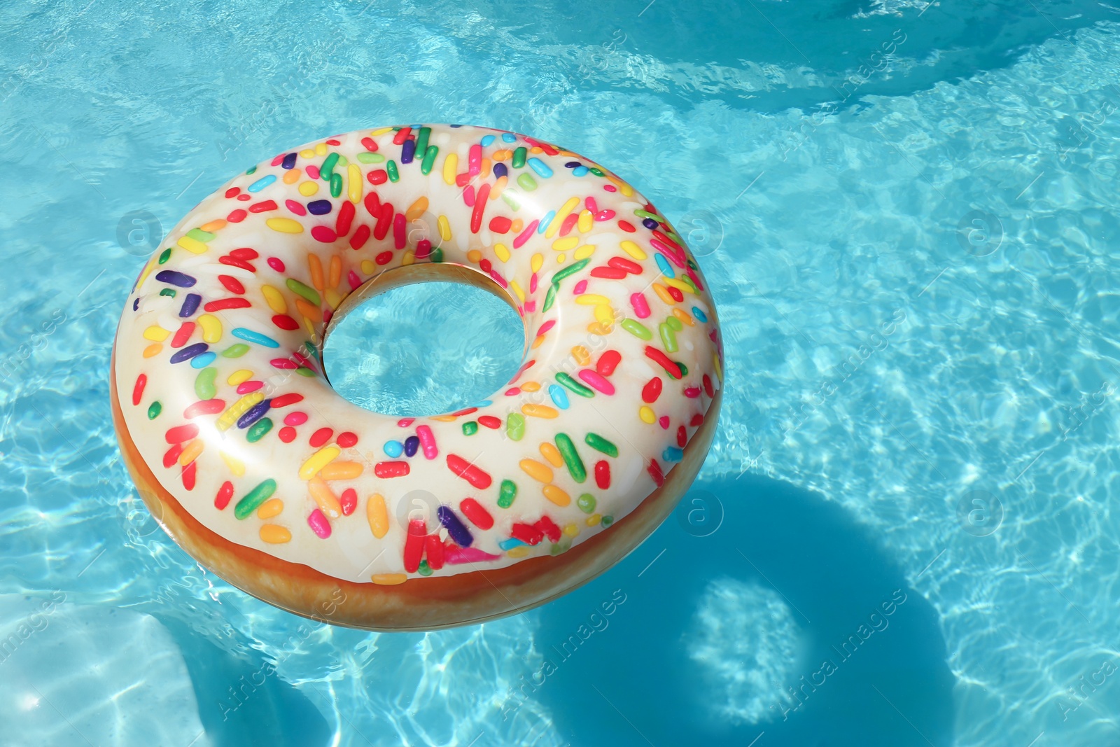 Photo of Bright inflatable doughnut ring floating in swimming pool on sunny day. Space for text