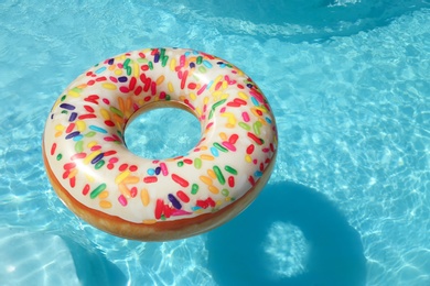 Bright inflatable doughnut ring floating in swimming pool on sunny day. Space for text