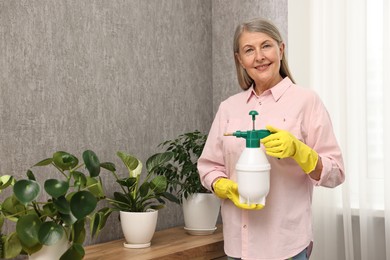 Photo of Happy housewife with plant mister near green houseplants at home