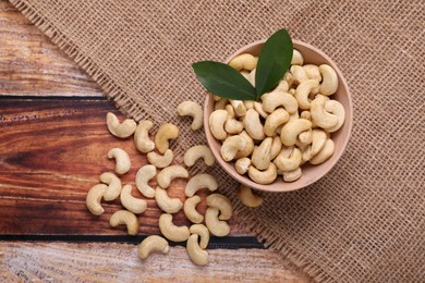 Photo of Tasty cashew nuts and green leaves on wooden table, top view