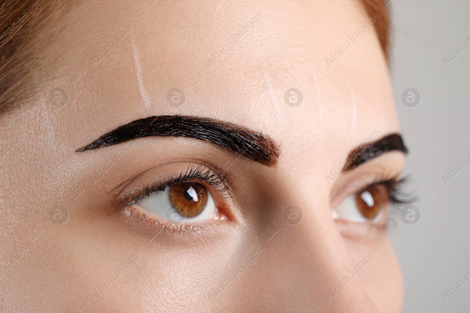 Photo of Woman during eyebrow tinting procedure on grey background, closeup