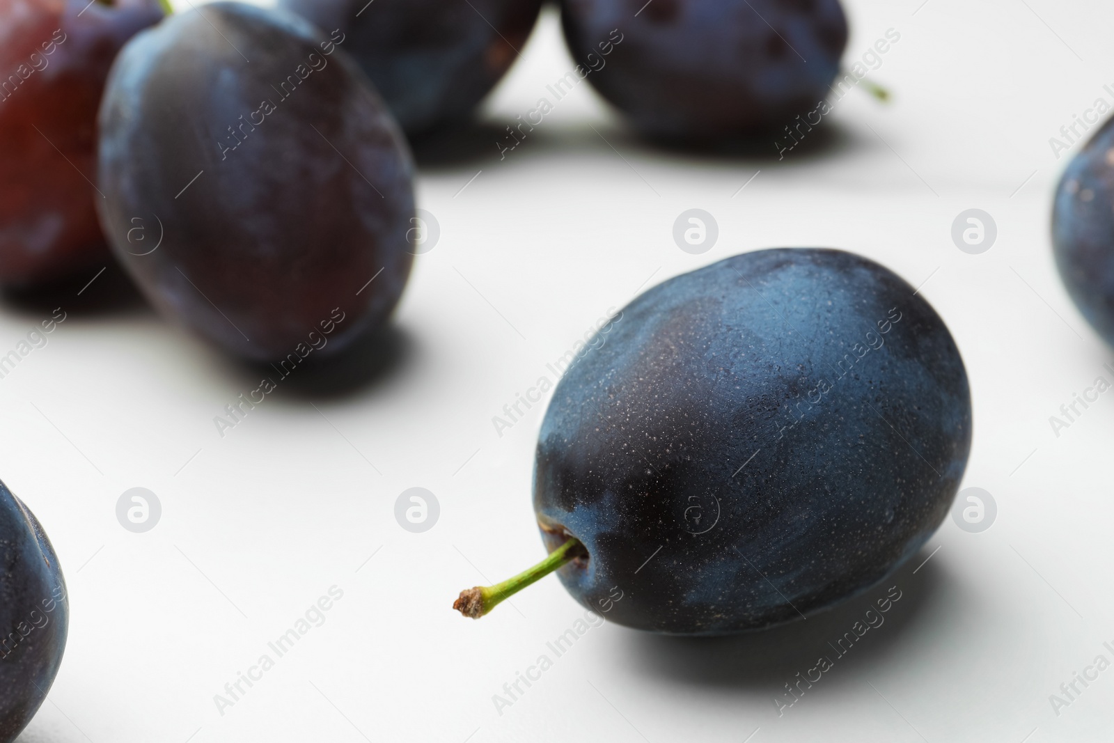 Photo of Many tasty ripe plums on white table, closeup