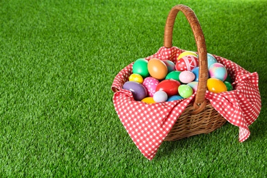 Photo of Wicker basket with Easter eggs on green grass. Space for text