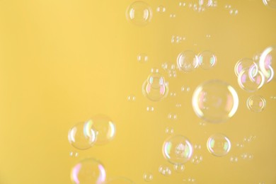 Photo of Beautiful transparent soap bubbles on yellow background
