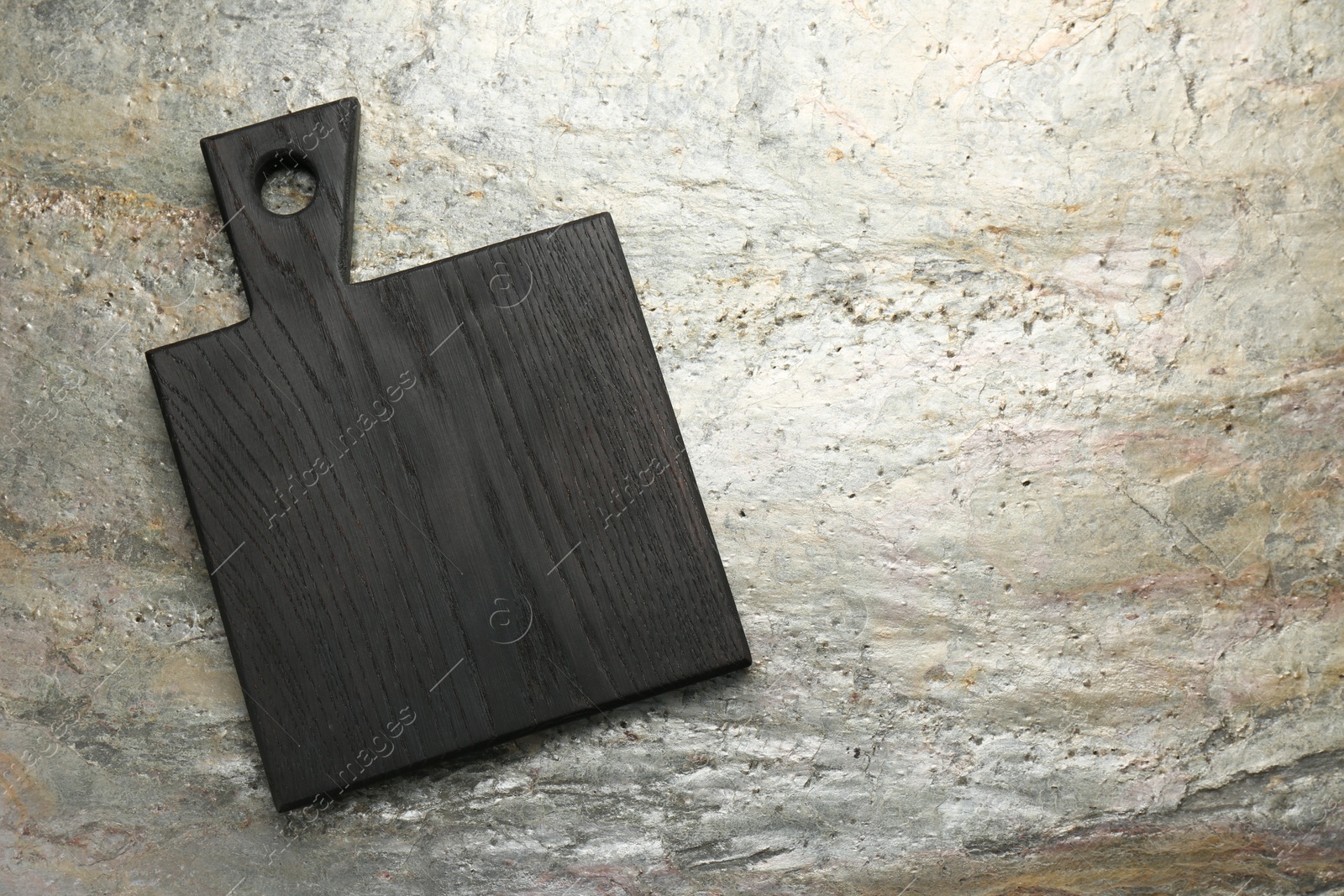 Photo of Black wooden cutting board on textured table, top view. Space for text