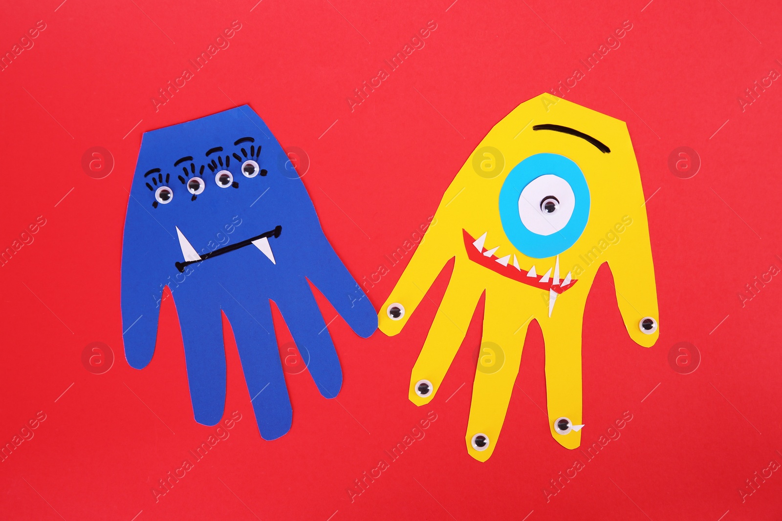 Photo of Funny hand shaped monsters on red background, flat lay. Halloween decoration