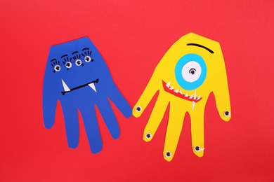 Photo of Funny hand shaped monsters on red background, flat lay. Halloween decoration