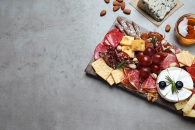 Wooden board with different appetizers on grey table, flat lay. Space for text