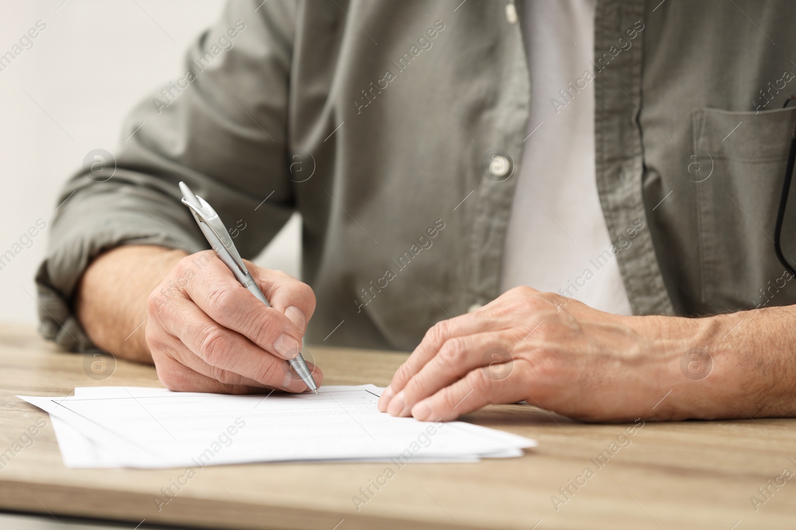 Photo of Senior man signing Last Will and Testament at wooden table indoors, closeup