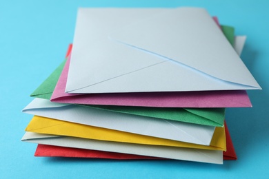 Stack of colorful paper envelopes on light blue background, closeup