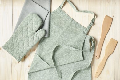 Photo of Kitchen napkin, apron, glove and spatulas on wooden table, flat lay