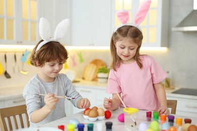 Easter celebration. Cute children with bunny ears painting eggs at white marble table in kitchen