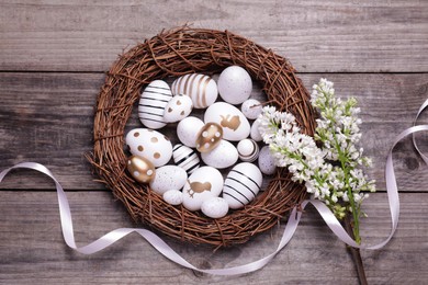 Many painted Easter eggs, branch of lilac flowers and ribbon on wooden table, flat lay