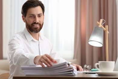 Photo of Happy man working with documents at wooden table in office. Space for text