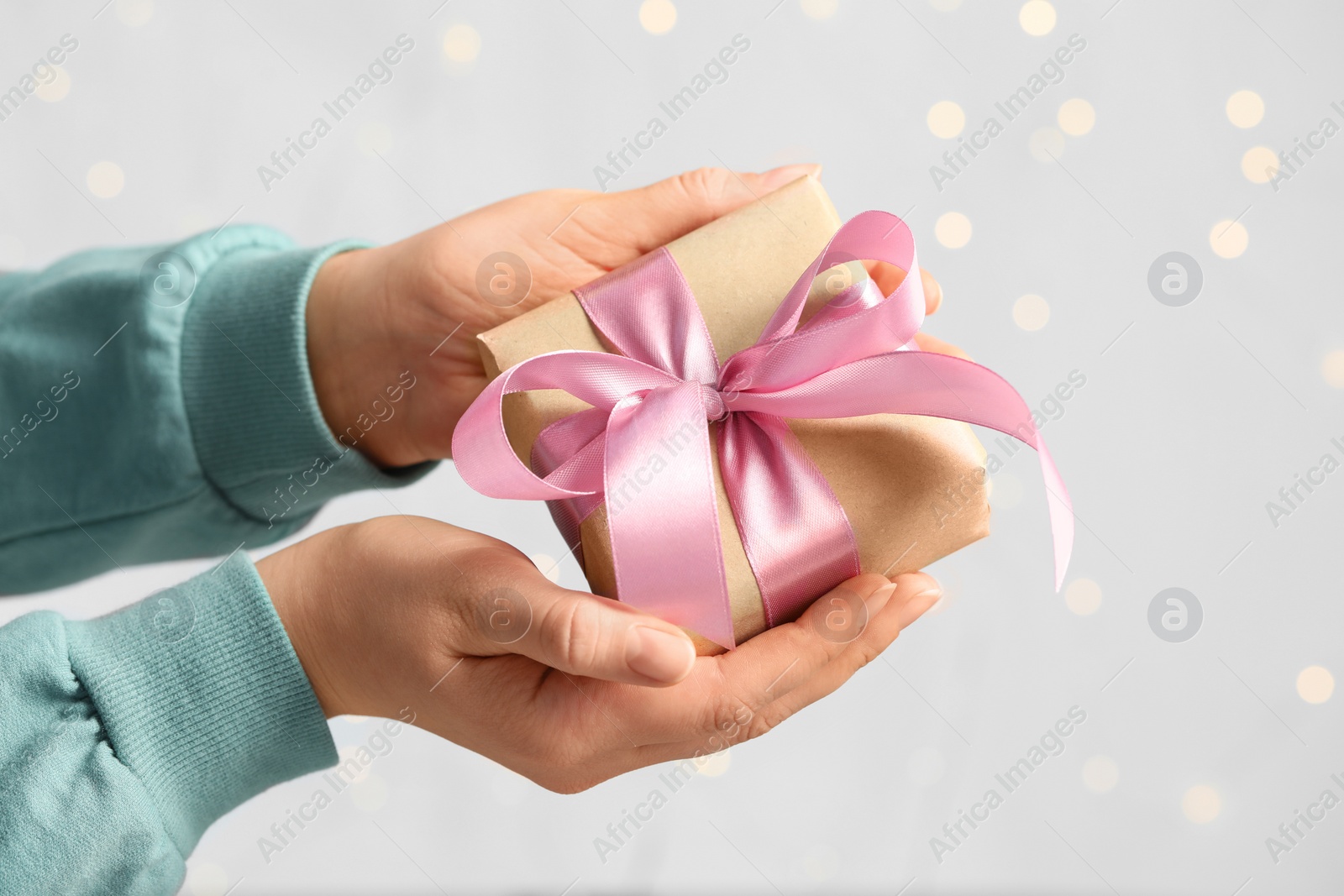 Photo of Woman holding gift box with pink bow against blurred festive lights, closeup. Bokeh effect