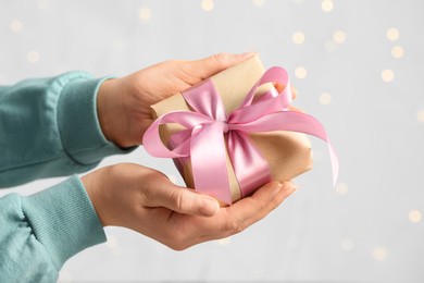 Woman holding gift box with pink bow against blurred festive lights, closeup. Bokeh effect