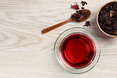 Cup of fresh hibiscus tea and dry flower leaves on wooden table, flat lay. Space for text