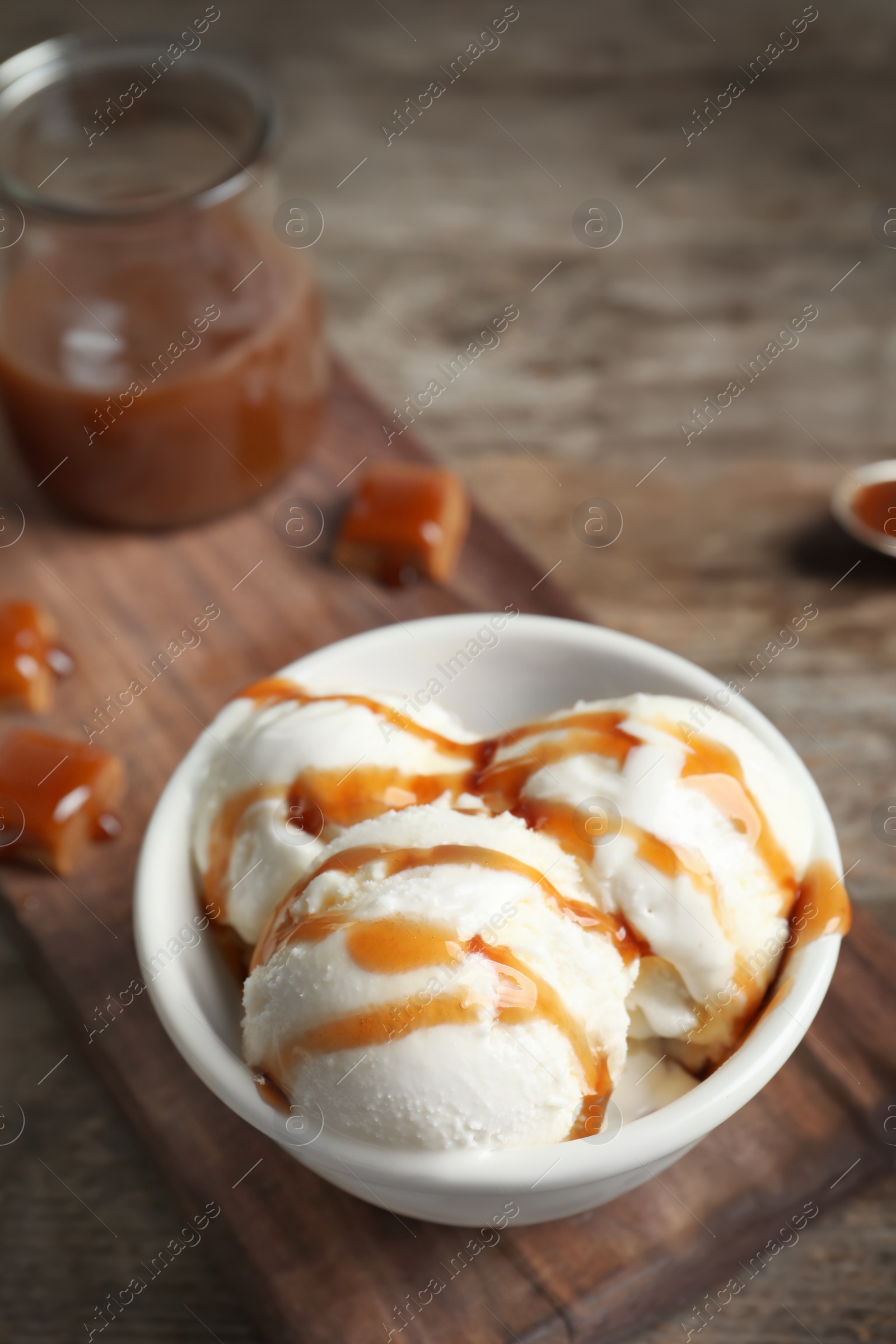Photo of Tasty ice cream with caramel sauce in bowl on wooden board