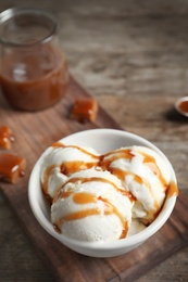 Tasty ice cream with caramel sauce in bowl on wooden board