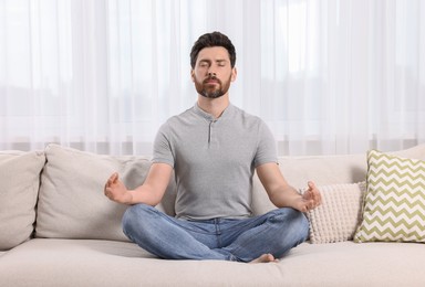 Photo of Man meditating on sofa at home. Harmony and zen