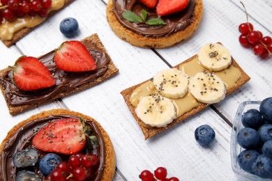 Fresh rye crispbreads and rusks with different toppings on white wooden table, closeup