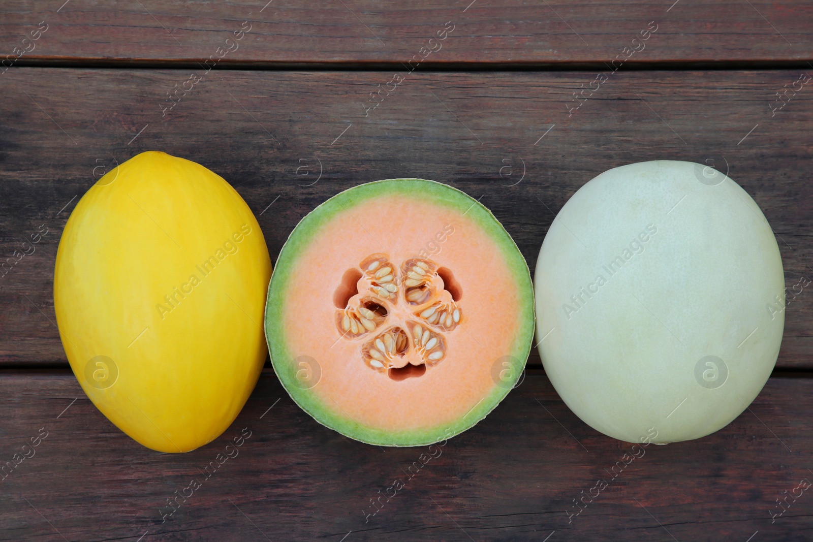 Photo of Different types of tasty ripe melons on wooden table, flat lay