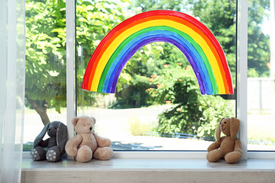 Photo of Painting of rainbow on window and toys indoors. Stay at home concept