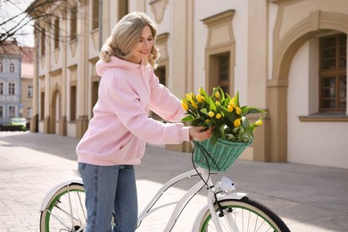 Beautiful woman with bicycle and bouquet of yellow tulips on city street