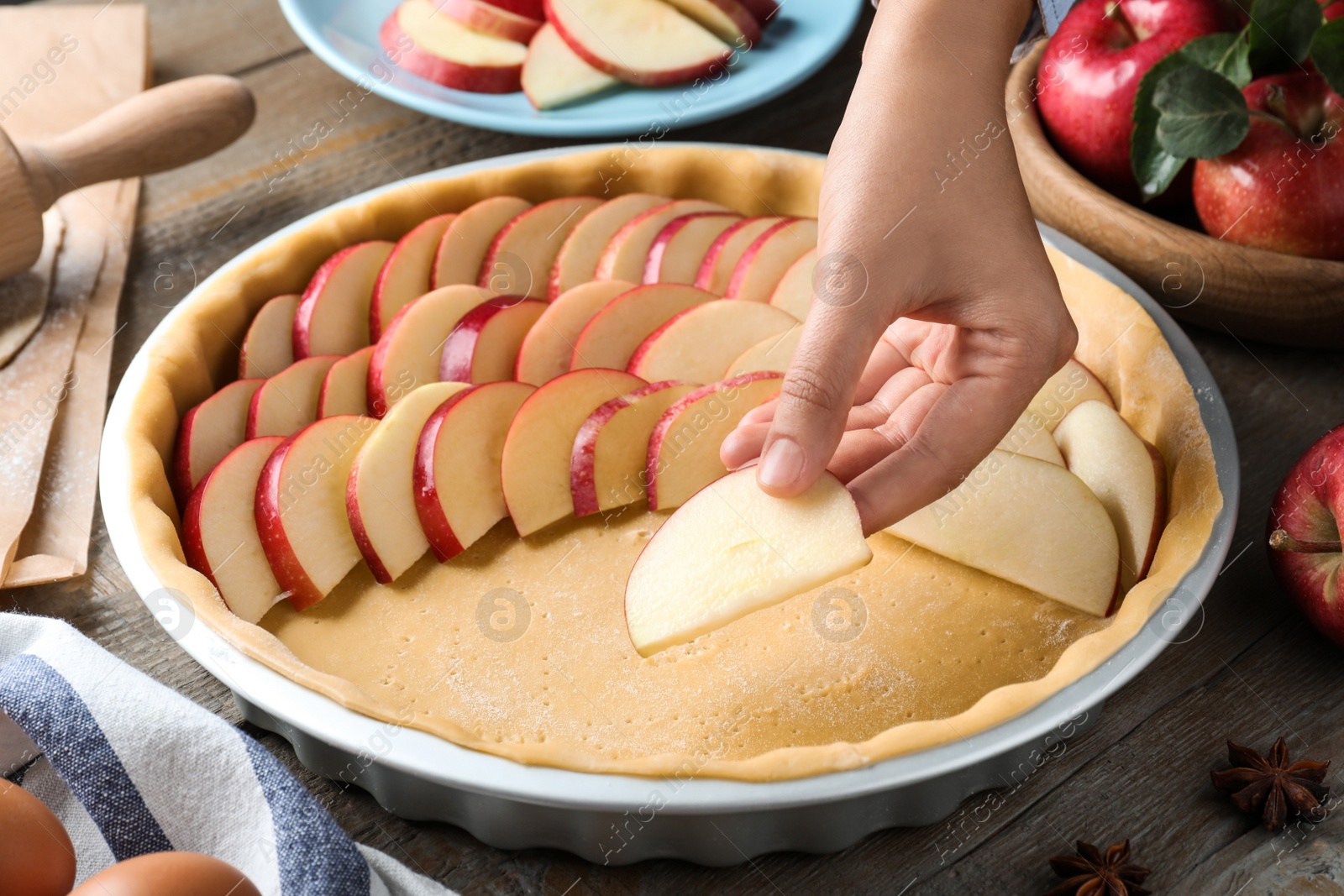 Photo of Woman putting apple slices into dish with raw dough at wooden table, closeup. Baking pie