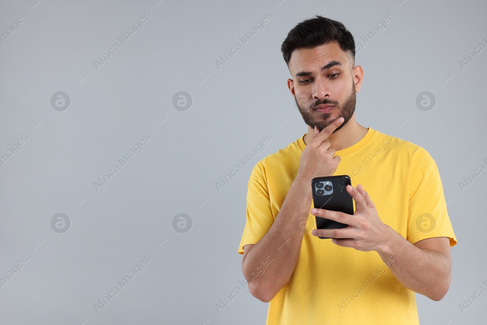 Photo of Handsome young man using smartphone on grey background, space for text