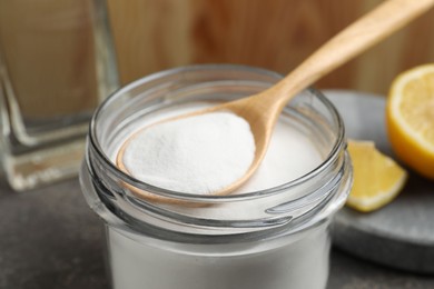 Photo of Baking soda, spoon and lemon on table, closeup