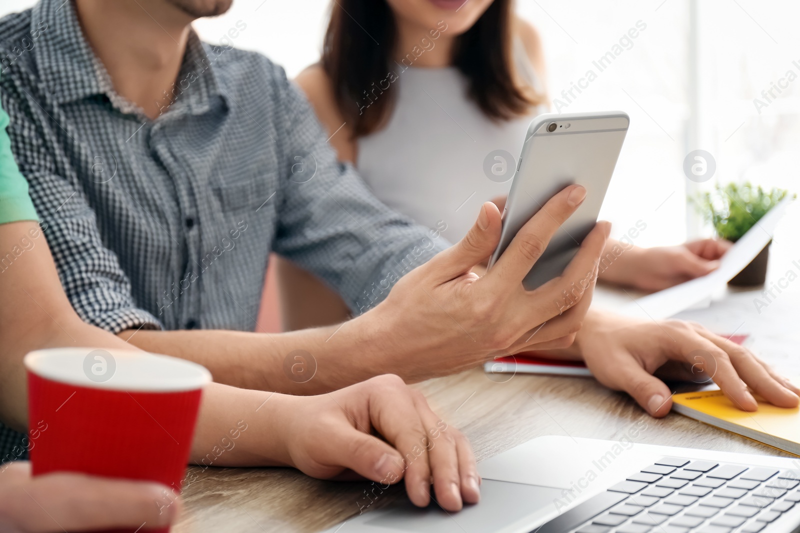 Photo of Young people using phone and laptop indoors, closeup