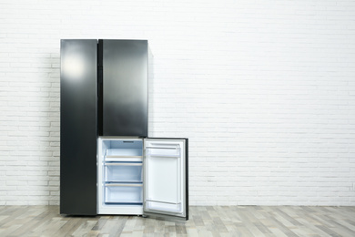 Photo of Modern empty refrigerator near white brick wall, space for text